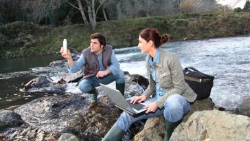 a two persons sitting at said of the river and hold laptop