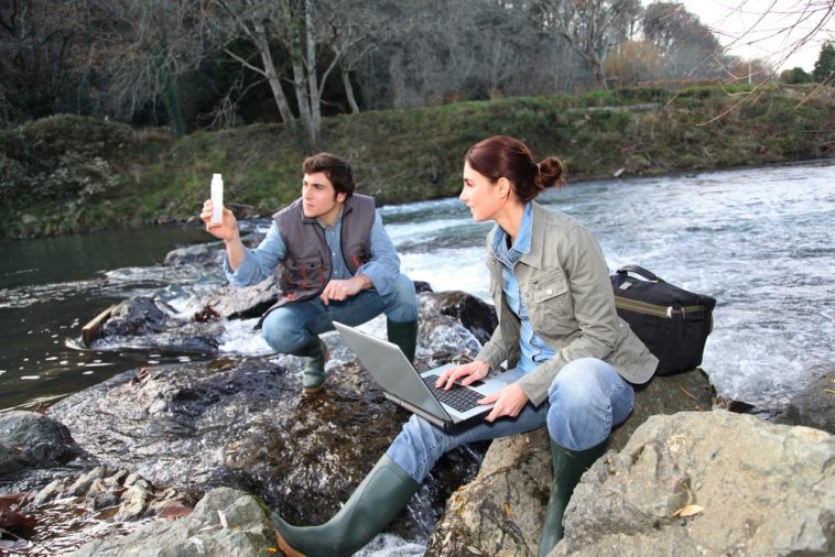 a two persons sitting at said of the river and hold laptop
